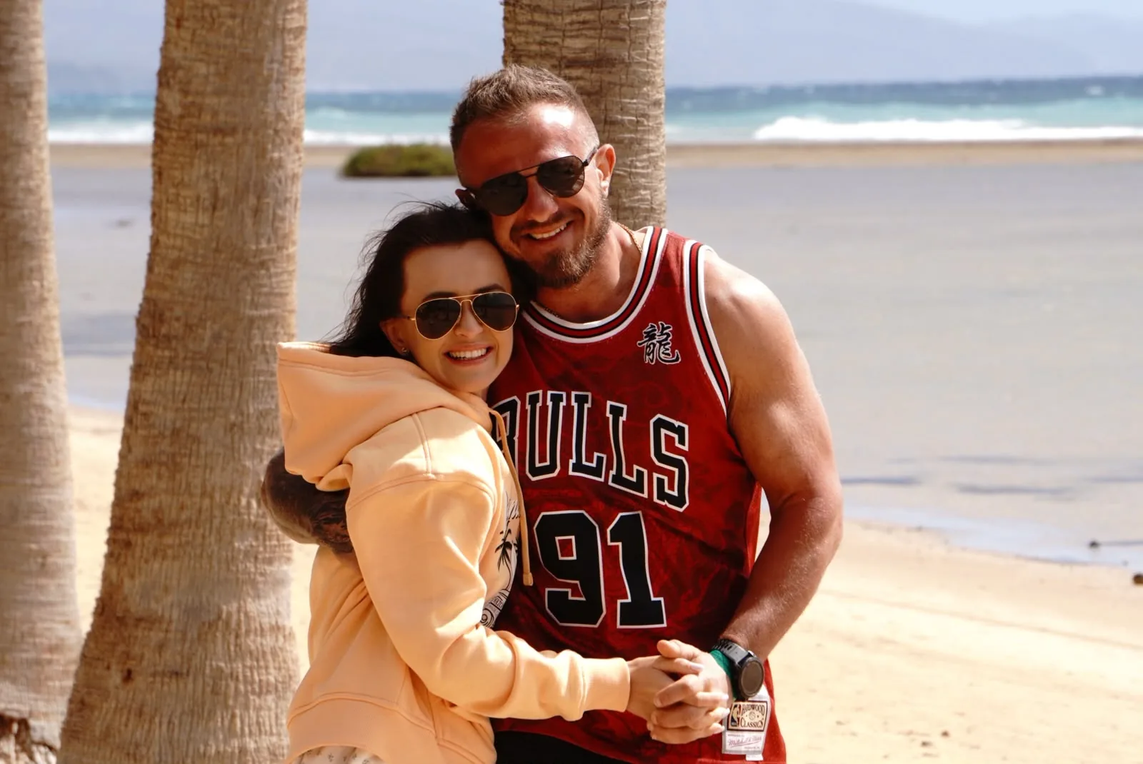 Pareja abrazada bajo las palmeras junto a la playa